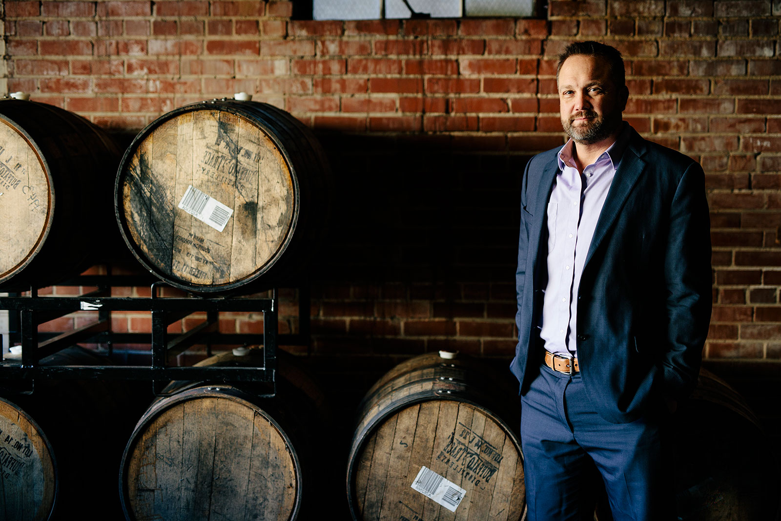 A man in a suit standing in front of barrels.